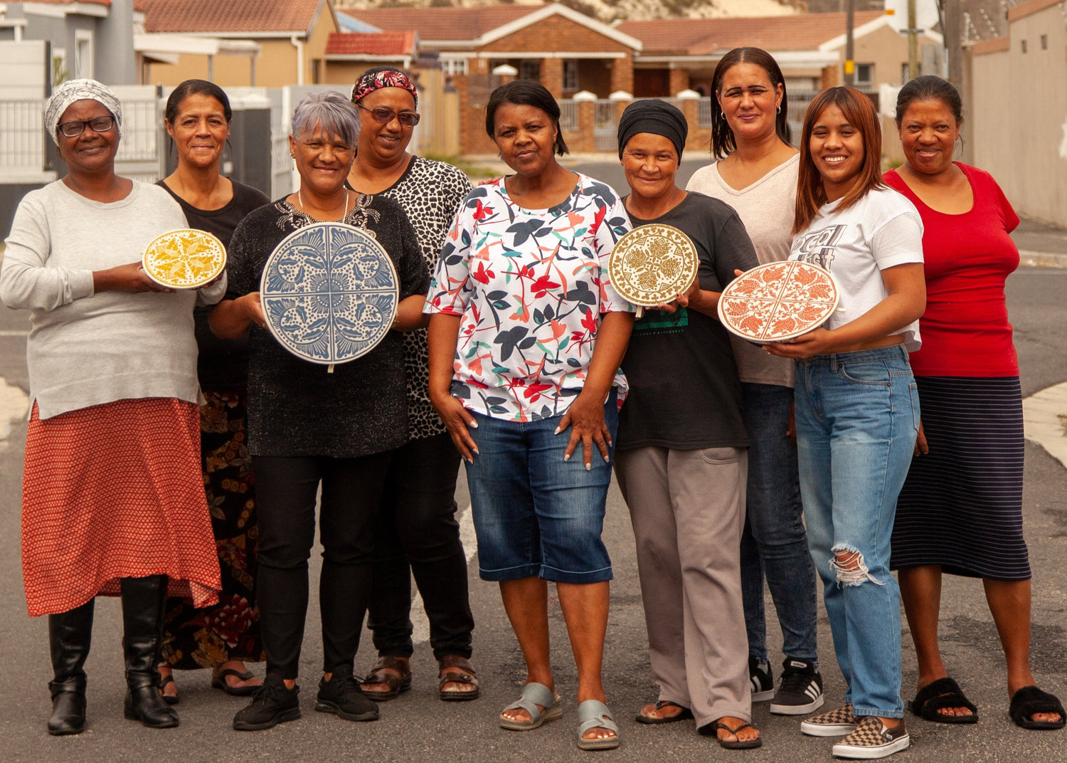 Group of women holding decorative plates outdoors with a residential area in the background